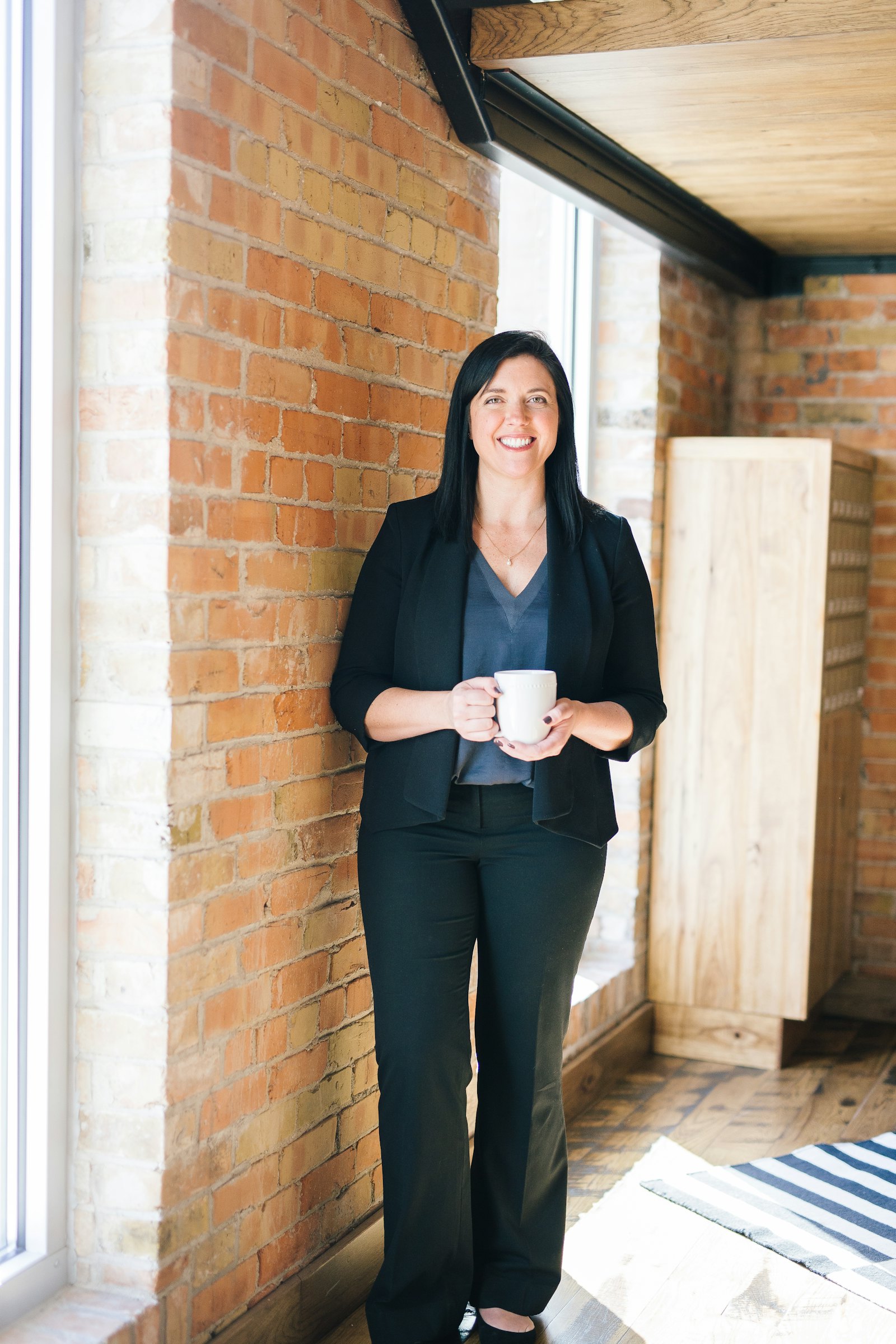 A planner in professional attire standing in a bright industrial-style office, holding a mug, representing the consultation setting.