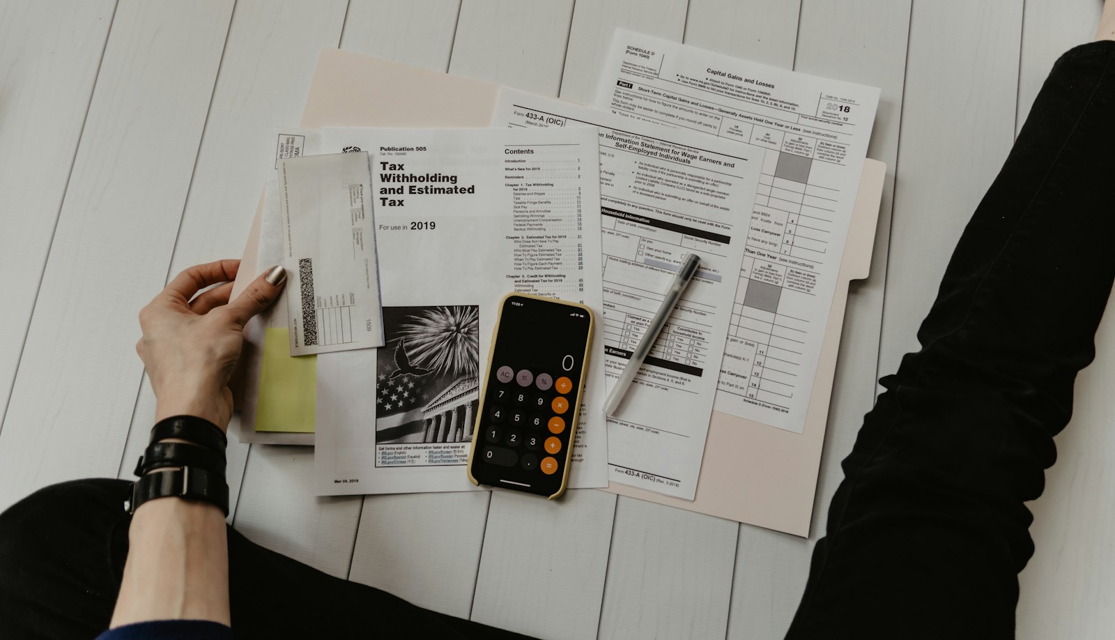 Hands working through financial paperwork with a calculator and pen on a light wooden surface, representing a planning review.
